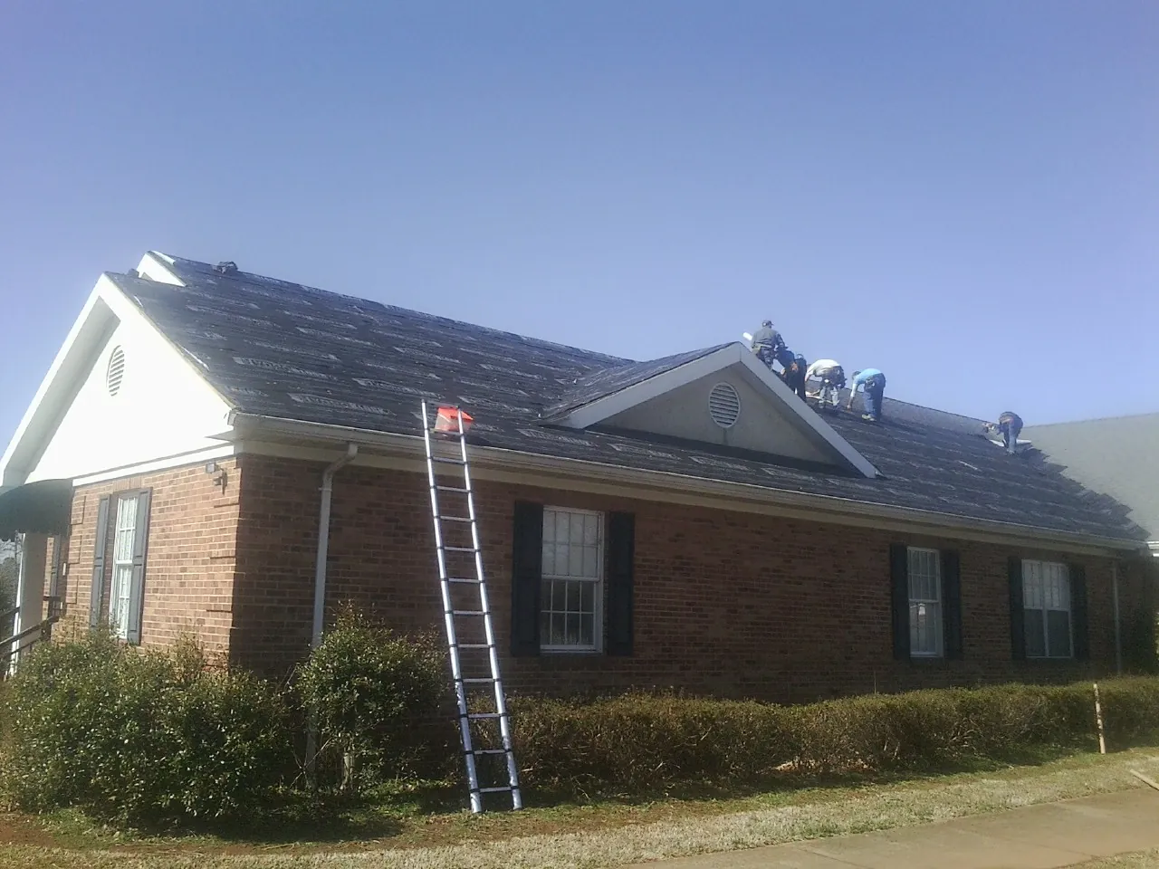 Crew tearing shingles off a brick ranch roof with a ladder set — Emergency Roof Repair work by our crew in Mayslick