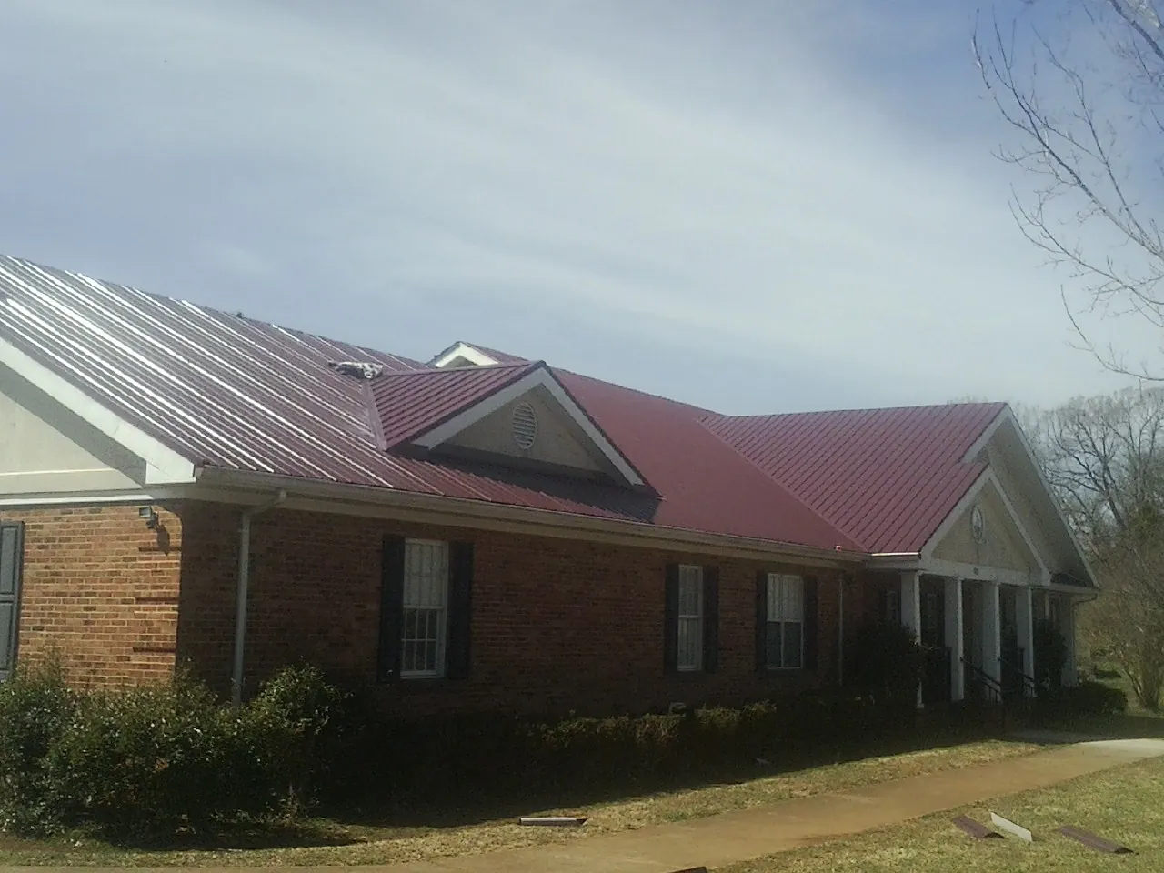 Red metal roof with gabled entries on a long brick building, from a Hail Damage Roof Repair job in Mayslick