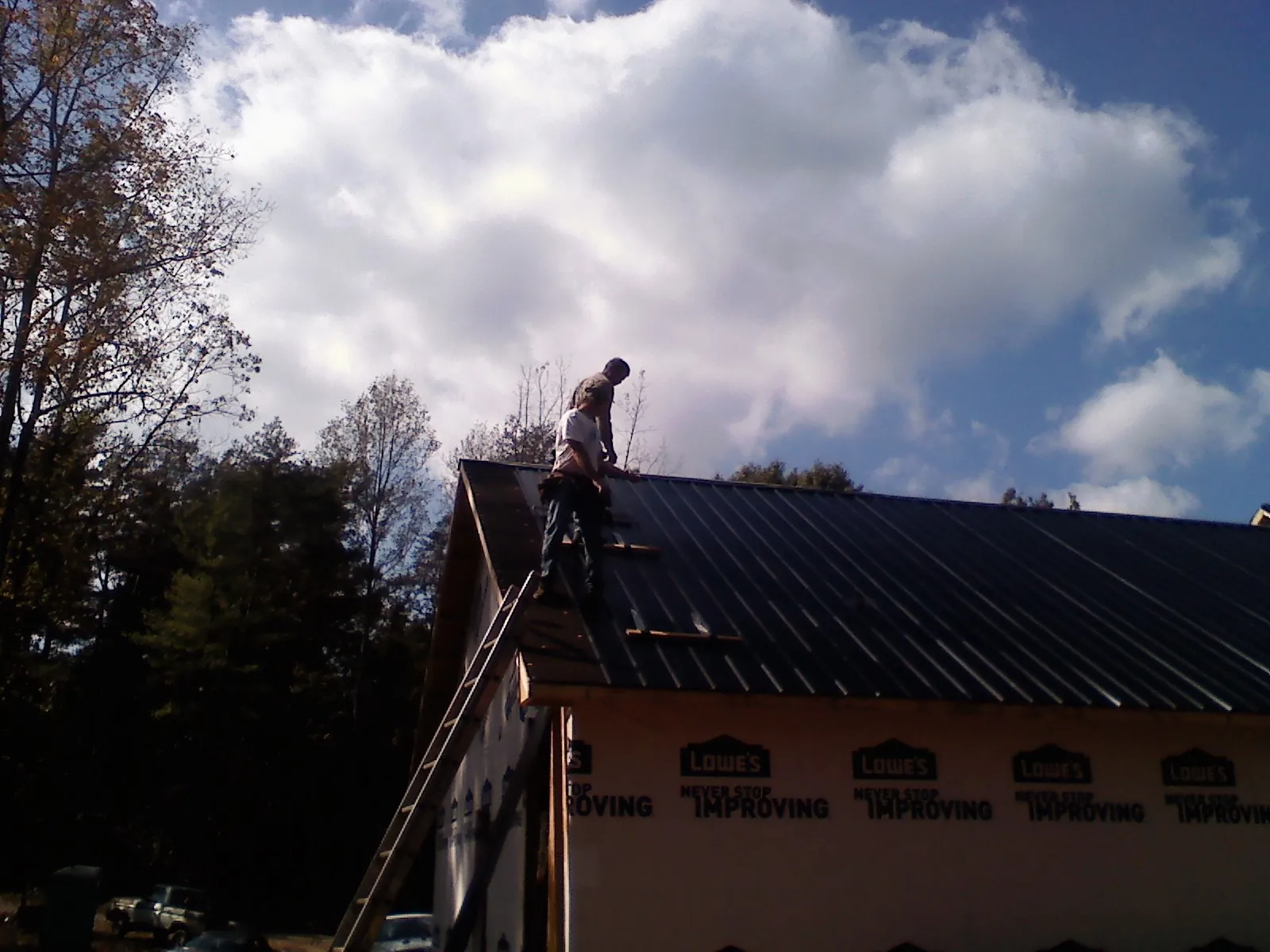 Roofer fastening dark metal panels high against a cloudy sky, from a Roof Inspection job in Mayslick
