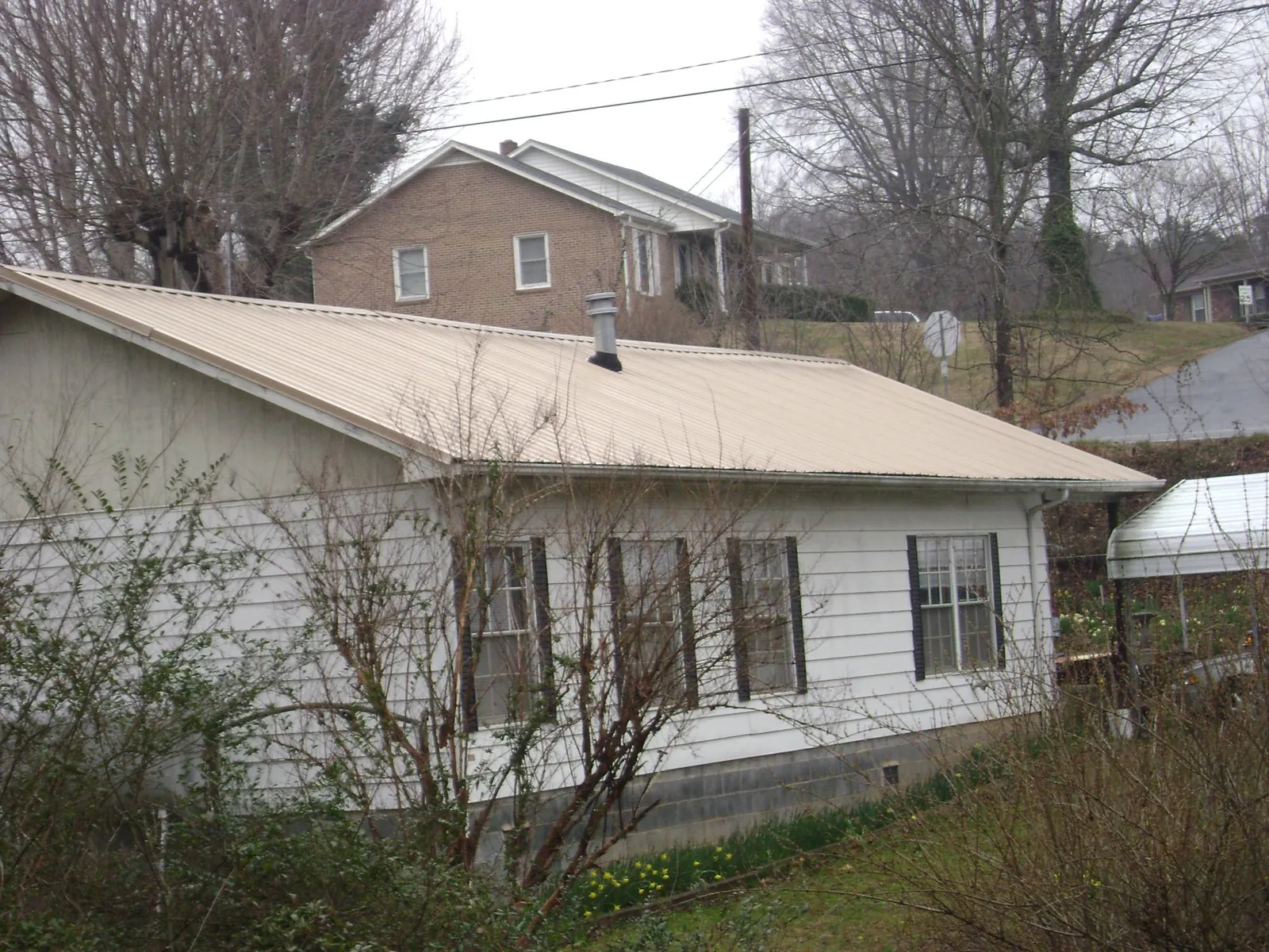 Tan metal roof on a white sided house set into a hillside — Commercial Roofing by Roofing Brothers in Mayslick